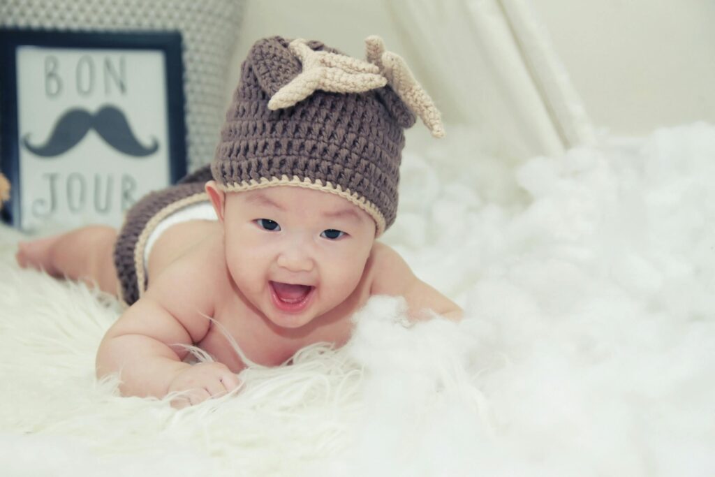 A joyful baby wearing a brown knitted hat lies on a soft surface, radiating happiness from best baby essentials store