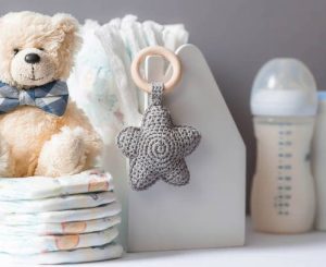 Wooden toys, a bear in a bow tie, a stack of diapers, bottles without labels and baby supplies on the changing table. Space for text.