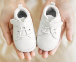 Tiny white baby shoes in man"u2019s hands. Closeup. Baby, pregnancy, parenting concept.